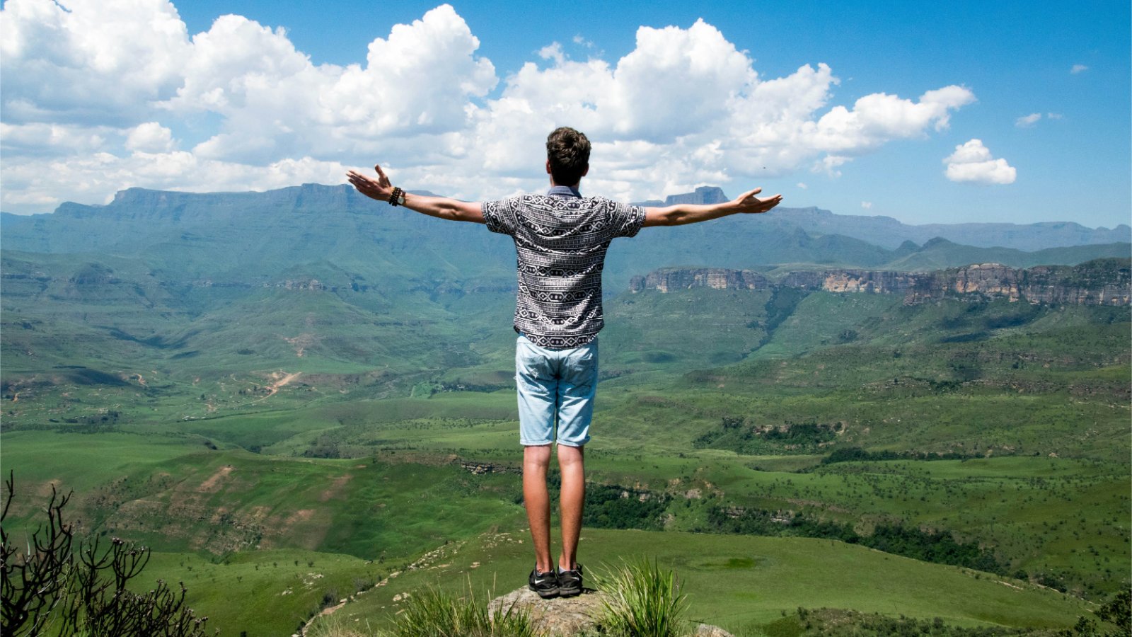 Mężczyzna stojący na szczycie góry, wyciągający ręce w geście triumfu.